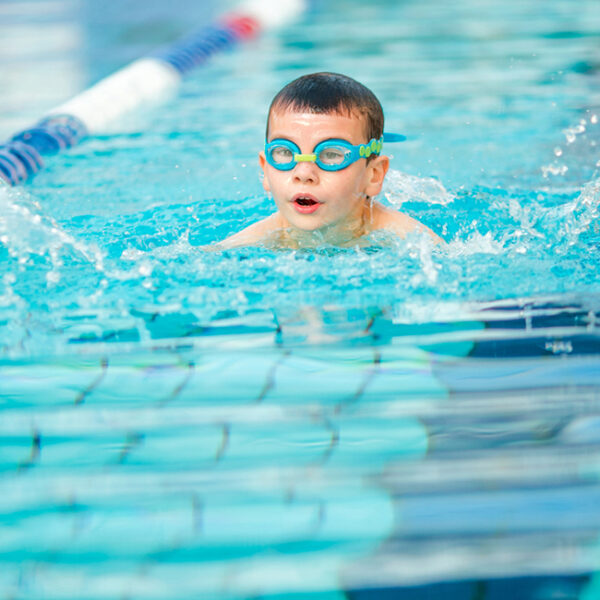 Ein Junge mit türkisfarbener Taucherbrille schimmt auf eine Bahn im Pool.